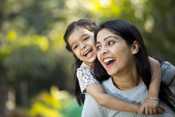 An adult has a child on their back and both are smiling.