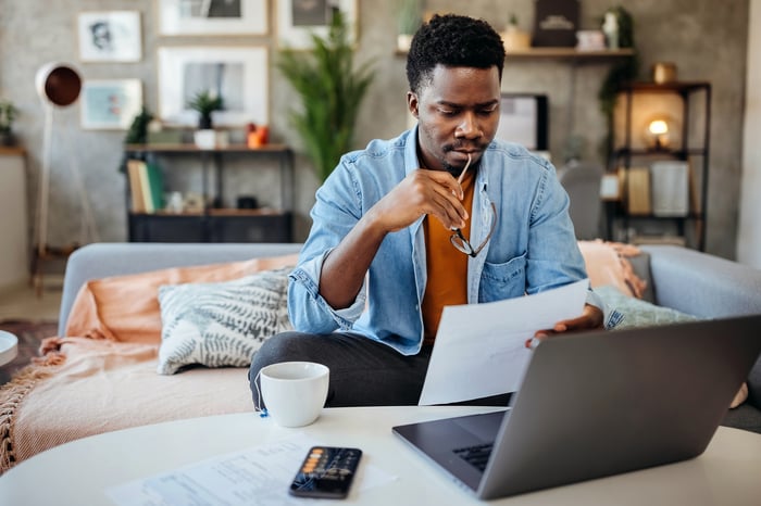 Person sitting at a table looking at paperwork and a laptop.