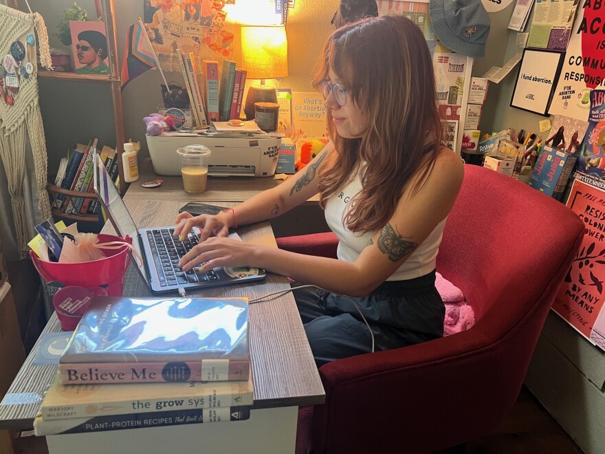 Woman sits at her desk working on a laptop. Abortion  rights posters are on the wall behind her.