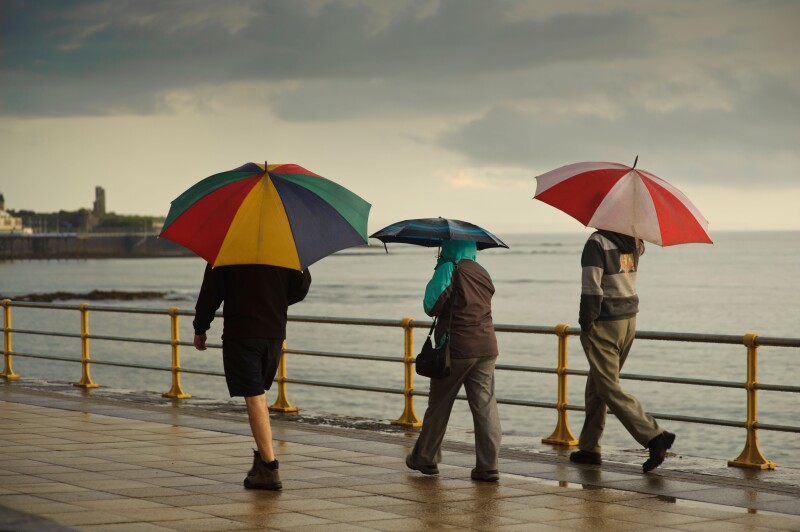 Three people sheltering under umbrellas on a wet summer evening, Aberystwyth Wales UK