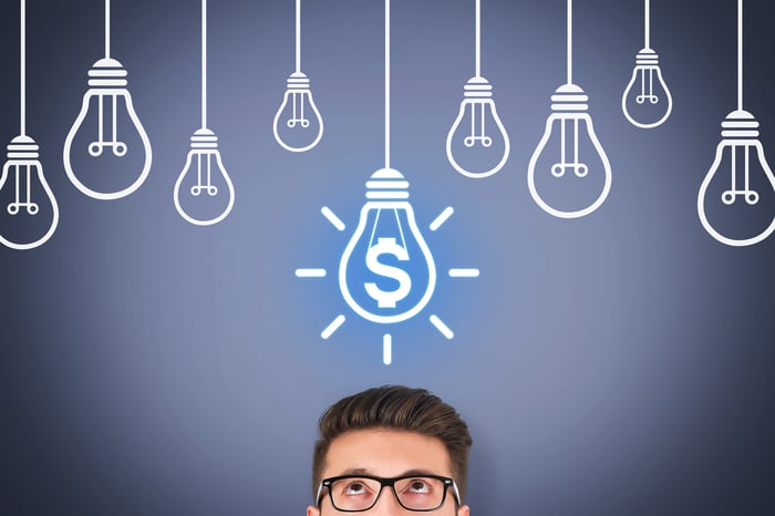 Person looking up at a cartoon lightbulb with a dollar sign inside it. 