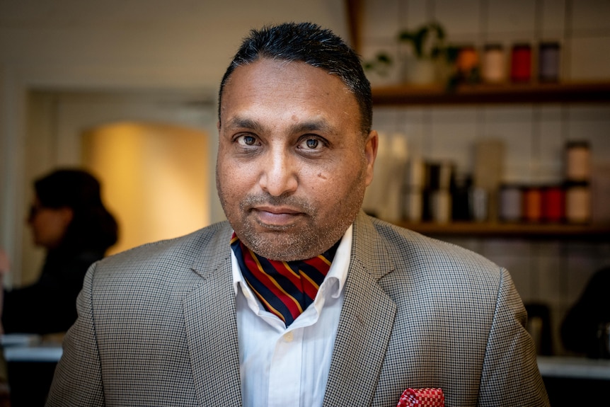 Lakhy Singh Saini sits at a table in a restaurant and smiles