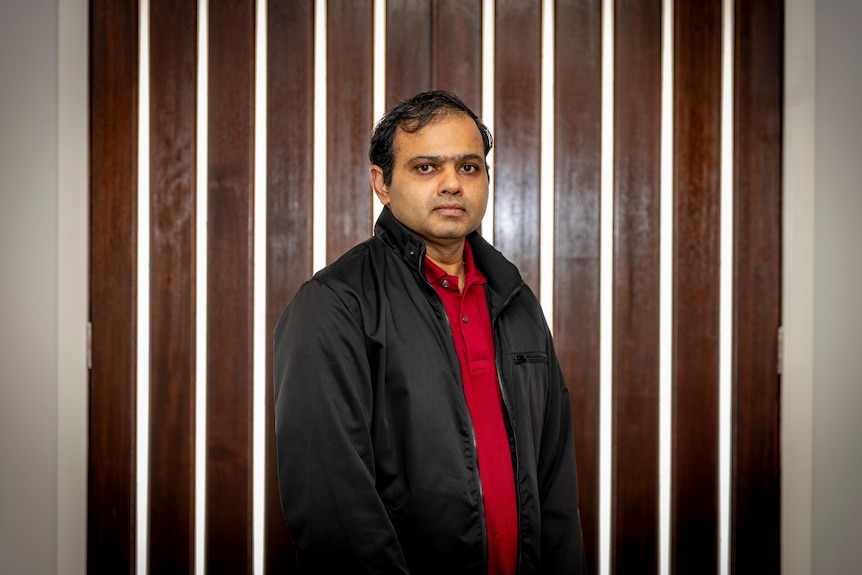 A man wearing a jacket with his hands in his pockets standing in front of wooden doors.