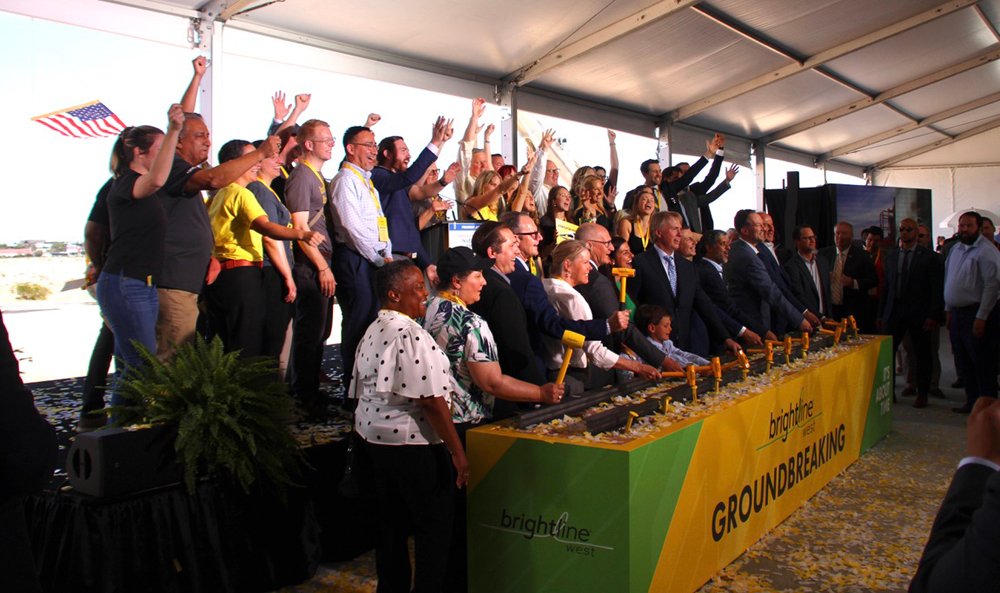 Group of people pose for photo behind "Brightline West Groundbreaking" banner