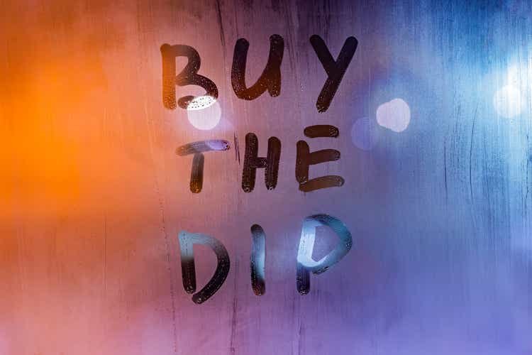 phrase buy the dip handwritten on night wet window glass surface