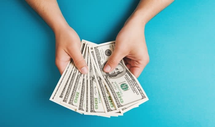 Person holding hundred dollar bills against a blue background.