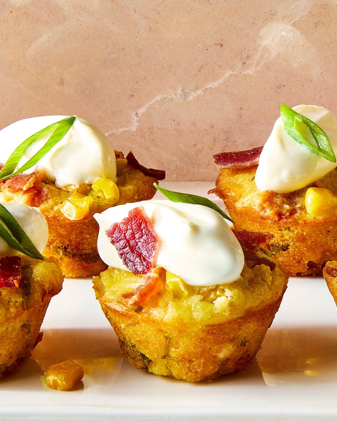 loaded cheesy corn bites topped with sour cream, sliced scallions, and bacon