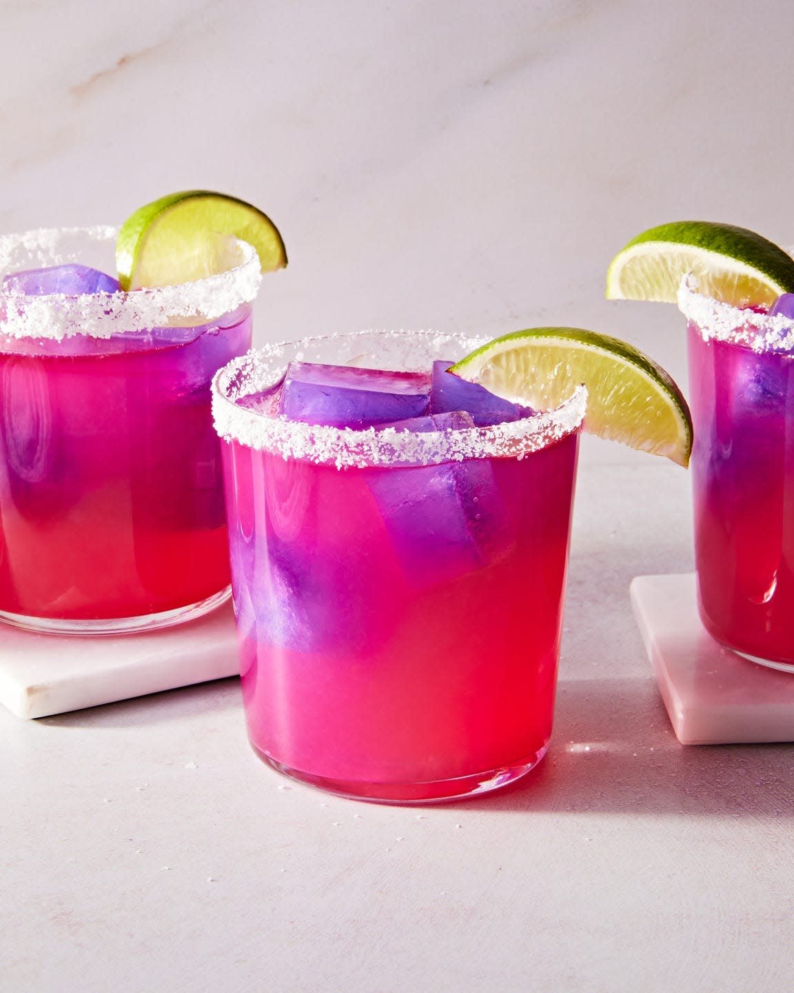 pink margarita with a purple ice cube with a salt rim and lime wedge