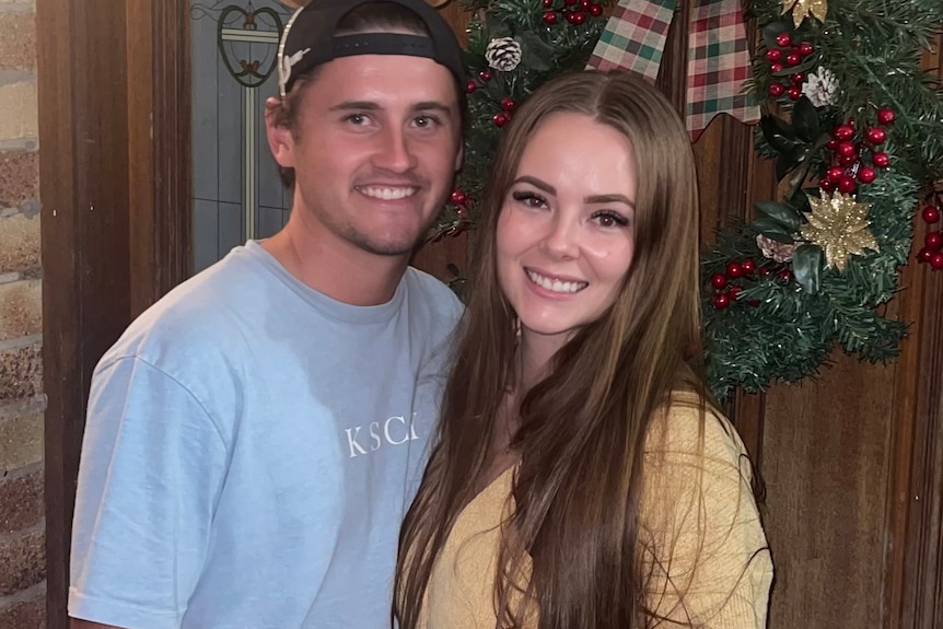 Thomas Bowness and Shannon Nielsen smile, standing in front of a door with a Christmas wreath.