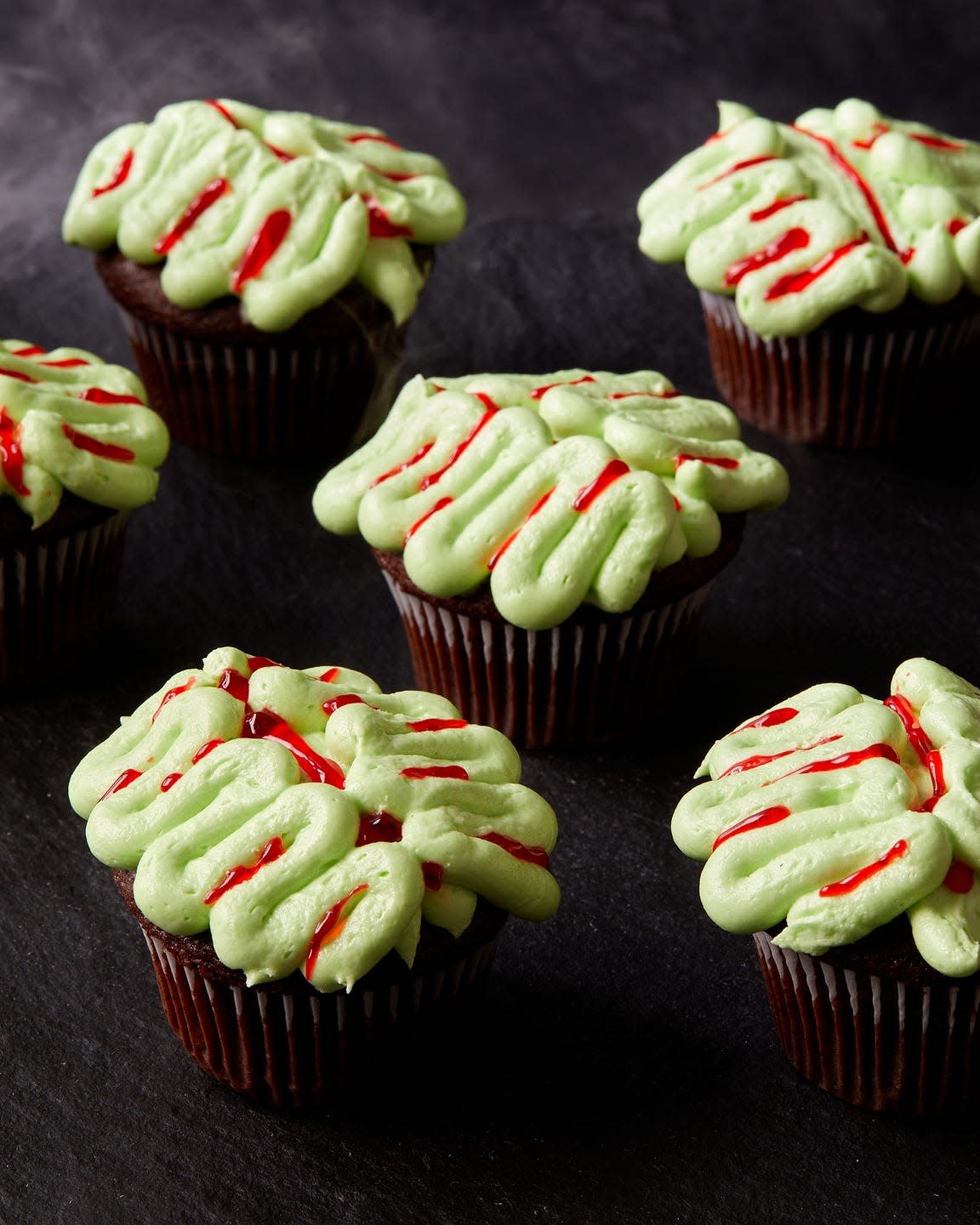 chocolate cupcakes decorated with green frosting and red gel food coloring to look like zombie brains