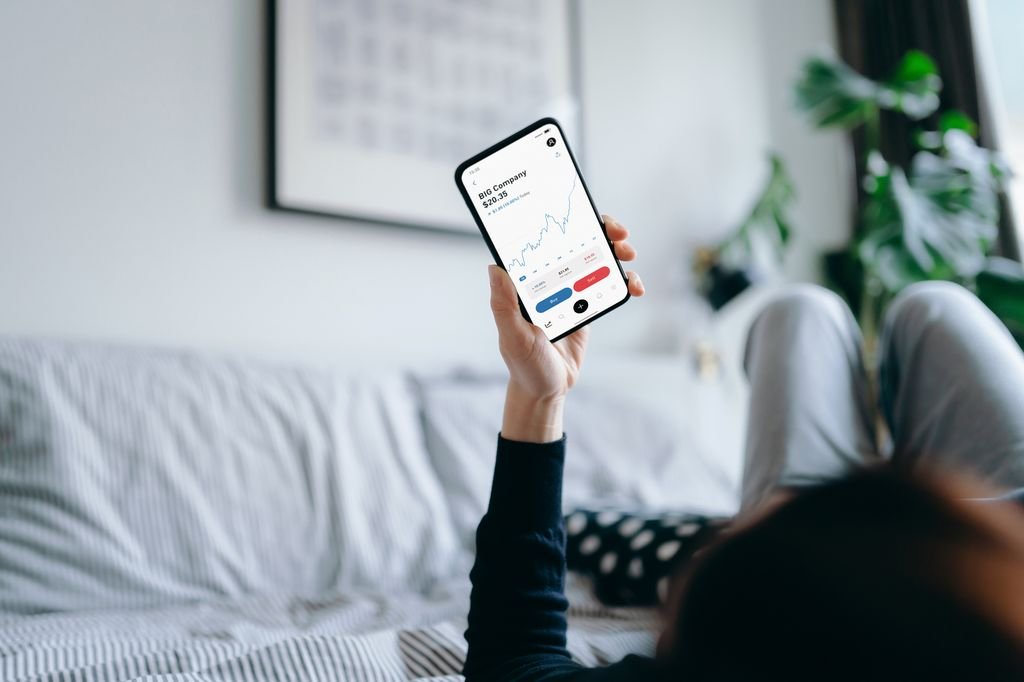 Young woman lying on bed at home, reading financial trading data on smartphone. Financial investment, stock market and exchange, accounting concept
