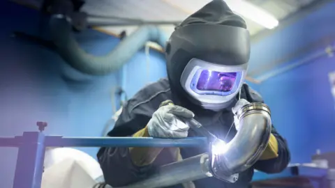 Getty Images A welder in protective clothing is welding a pipe
