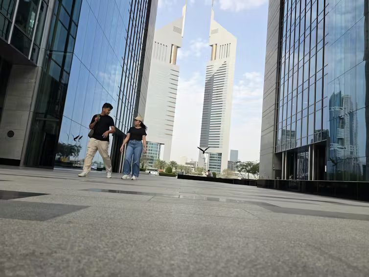 a young man and woman walk past an otherwise deserted nasdaq dubai in dubai financial centre in the UAE.