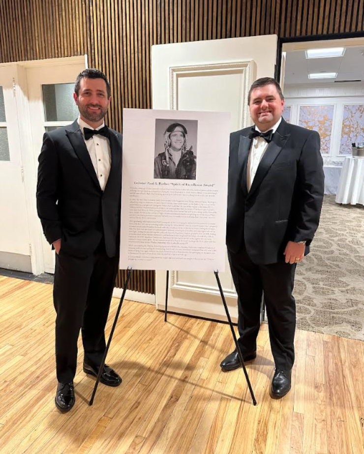 Planners Taylor Pankratz (left) and Jason Barber (right) posed next to a picture of their late grandfather, Air Force Col. Paul Barber, at the March 2024 Aviators Ball in Nacogdoches, Texas. Their RIA sponsored the event and an aviation scholarship in their grandfather's name.