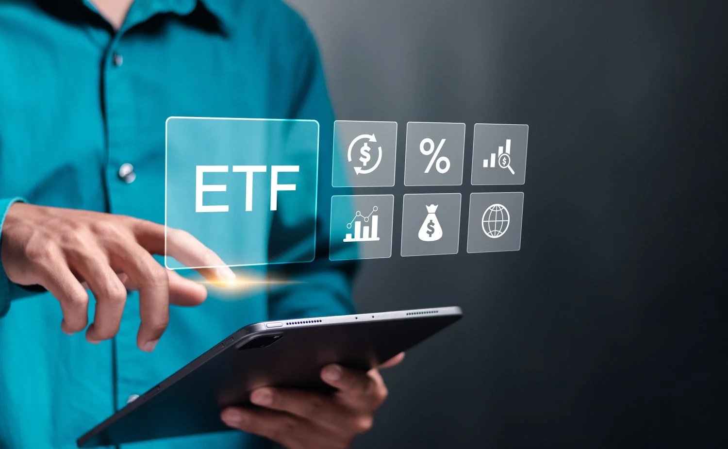A person wearing a teal shirt interacts with a glowing, holographic 'ETF' button on a translucent screen. Their right index finger touches the button, with a bright light emanating from the point of contact. Their left hand holds a dark tablet device. Arranged to the right of the 'ETF' button are six other translucent square icons representing financial concepts: currency exchange, a percentage sign, a bar chart with a magnifying glass, a different bar chart, a money bag with a dollar sign, and a globe. The background is dark and subtly blurred.