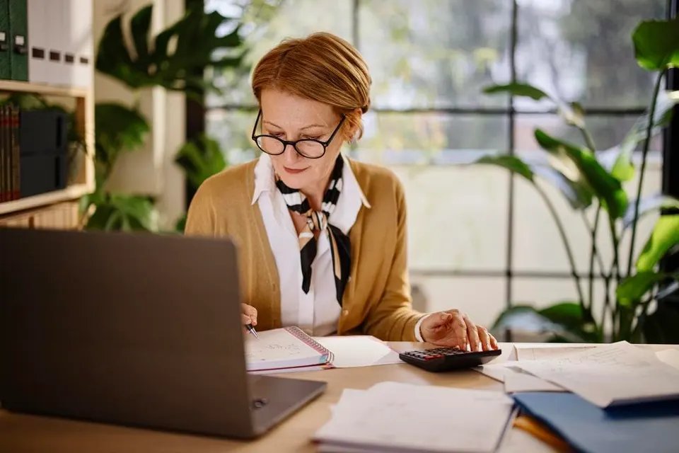 Middle aged woman calculates finances while in a home office.