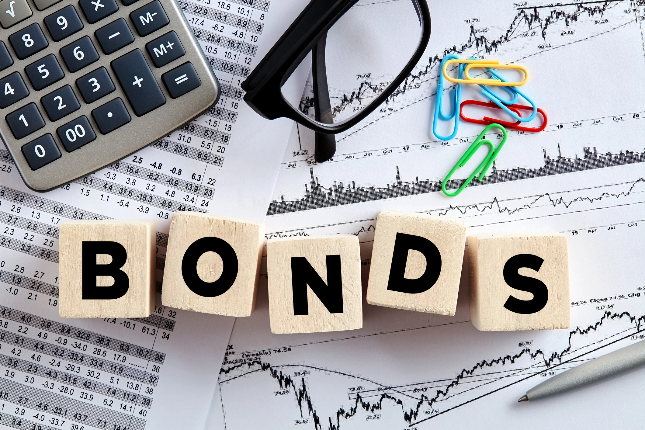 "Bonds" written on blocks near a calculator, a pair of glasses, and paper clips.